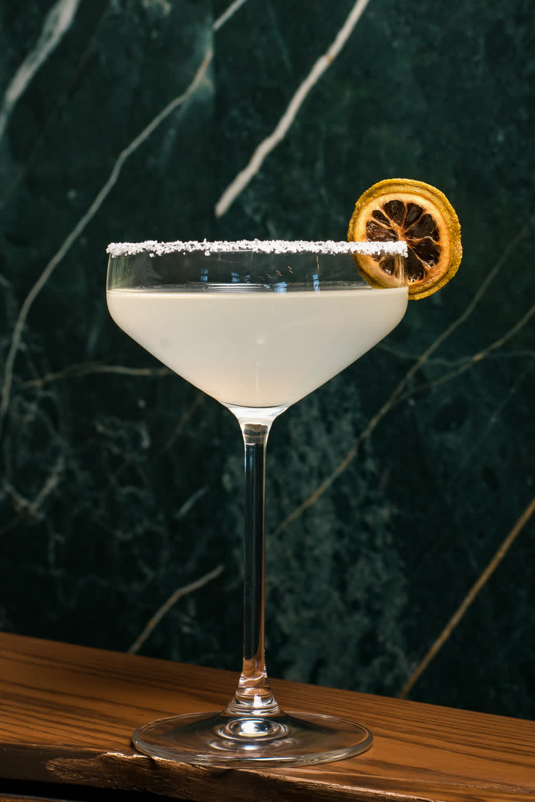 Salt-rimmed cocktail in a coupe glass against green marble